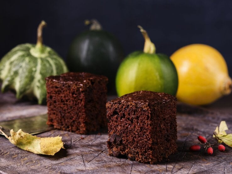 Im Hintergrund sind Zucchinis aus dem Garten zu sehen, vorne zwei schmackhafte Browsnies aus Schokolade und Zucchini.