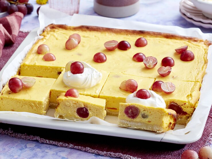 Kürbis-Trauben-Cheesecake Ein weißes Blech mit dem Kürbis-Trauben-Cheesecake auf einem blau-weißem Marmortisch von schräg oben fotografiert