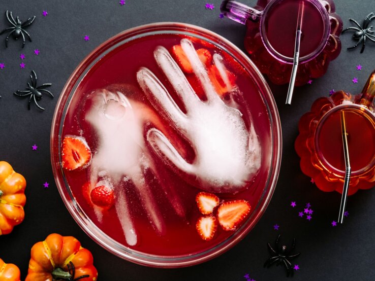 alkoholfreie Halloween-Bowle Draufsicht auf eine blutrote Fruchtbowle, in der eine gefrorene Hand aus Wasser liegt.