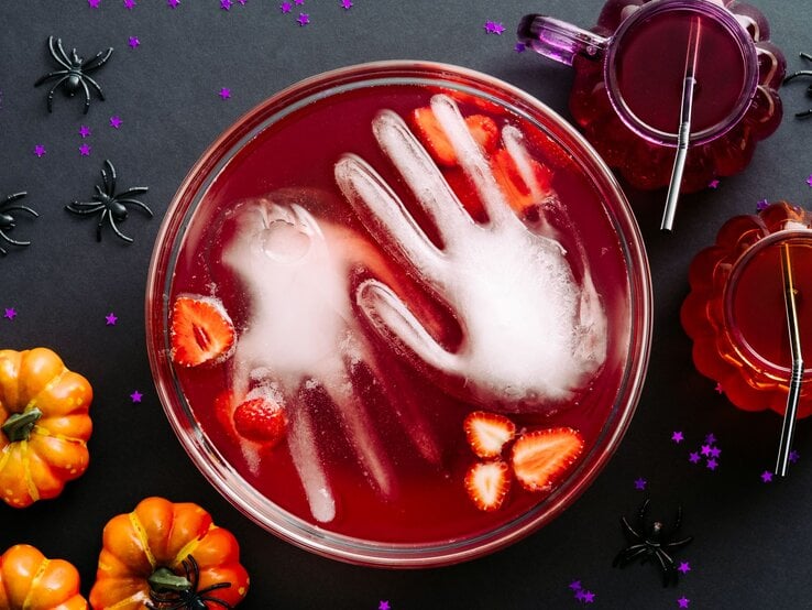 alkoholfreie Halloween-Bowle Draufsicht auf eine blutrote Fruchtbowle, in der eine gefrorene Hand aus Wasser liegt.