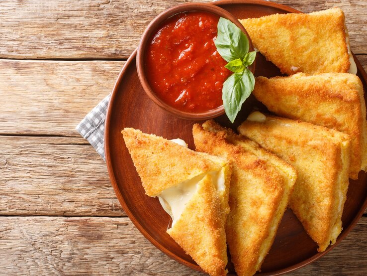 Italienisches-Grilled-Cheese-Sandwich Das Sandwich auf einem braunen Teller und Holztisch mit einem Schälchen Tomatensoße serviert. Alles direkt von oben fotografiert.