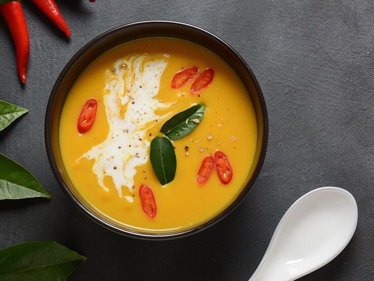 Eine dunkle Schale mit der orangen Suppe auf einem grauen Tisch direkt von oben fotografiert