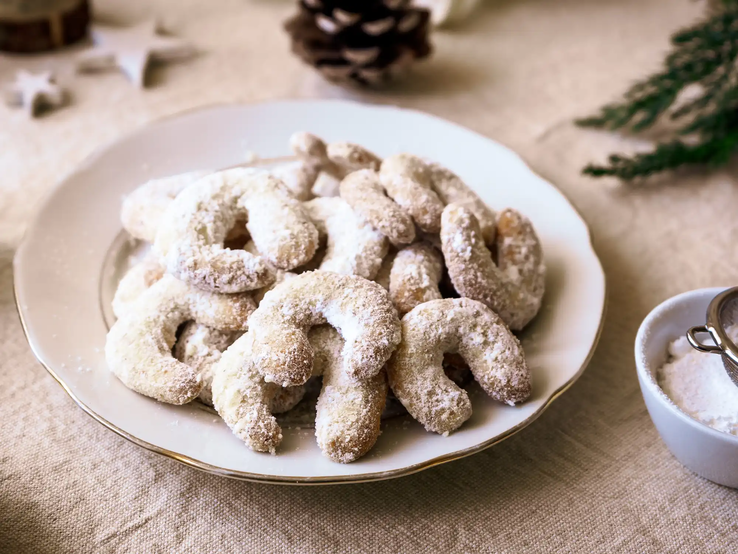 Die besten Vanillekipferl - unser Rezept von Oma Vanillekipferl auf Teller mit weihnachtlicher Deko auf dem Tisch
