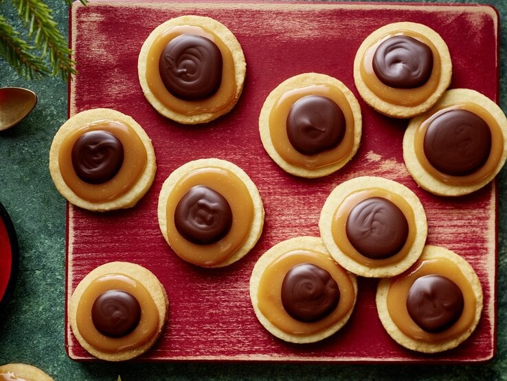 Die Toffifee-Taler auf einem rötlichen Schneidebrett und weihnachtlicher Deko drumherum. Alles direkt von oben fotografiert.