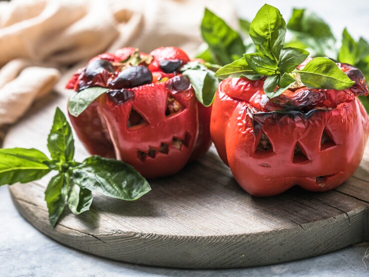 Halloween gefüllte Paprika Zwei geschmorte Paprika im Halloween-Look auf einem Holzbrett mit Basilikum dekoriert. Alles von der Seite und recht nah fotografiert.