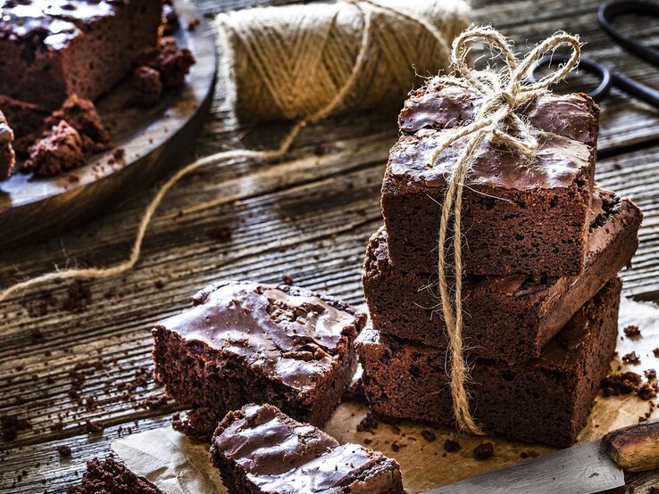 Klassische Brownies, mal einzeln, mal gestapelt / Untergrund grobes Holz /  Messer aus Metall / Kuchengitter / 