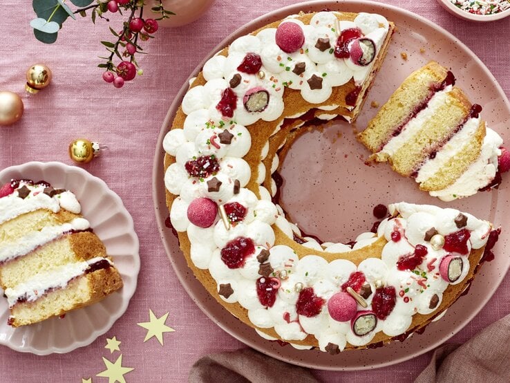 Die angeschnittene Torte auf einer rosa Tischdecke mit viel weihnachtlicher Dekoration. Alles direkt von oben fotografiert.