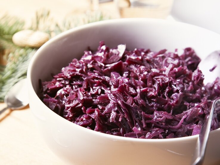 Eine weiße Schale mit dem Rotkohl auf einem hellen Holztisch von schräg oben fotografiert.