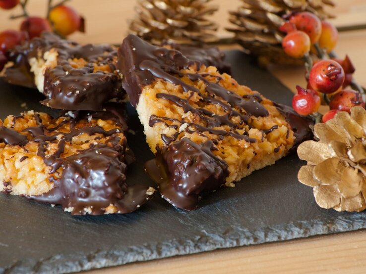 Klassische Nussecken mit Mürbeteig, karamellisierter Nuss-Schicht und Schokoladendekor, arrangiert auf einer Schieferplatte mit weihnachtlicher Dekoration.