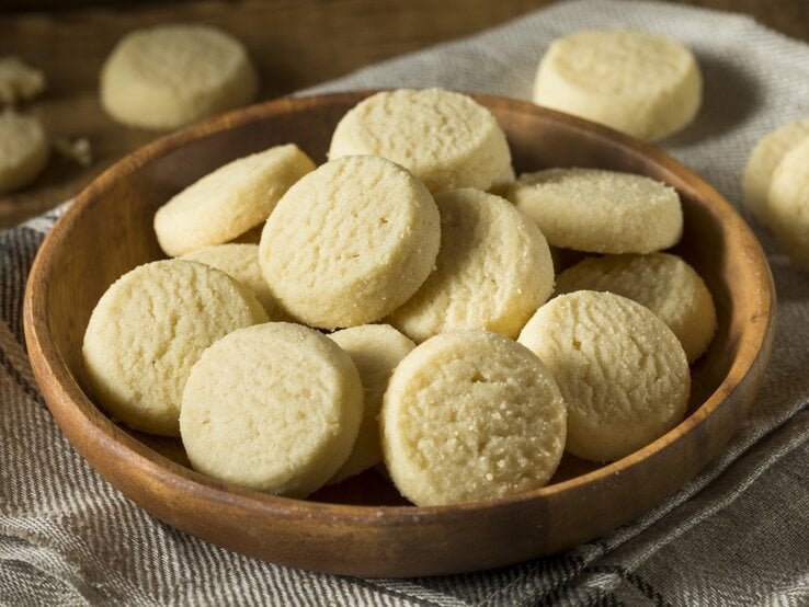 Runde Heidesand-Plätzchen in einem runden Schale aus Ton / Drumherum weitere Kekse / Draufsicht, schräg