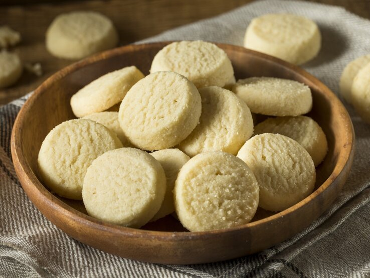Runde Heidesand-Plätzchen in einem runden Schale aus Ton / Drumherum weitere Kekse / Draufsicht, schräg