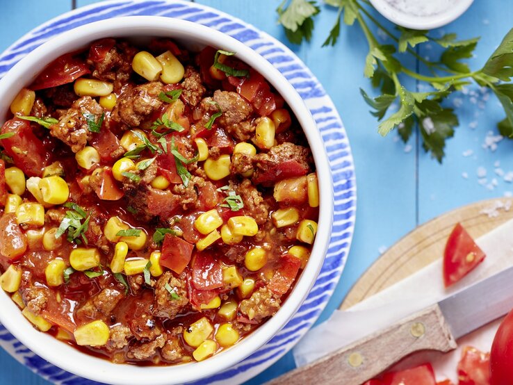 Eine Schale Chili con Carne in einem weiß-blauen Teller auf dem blauen Tisch. Alles direkt von oben fotografiert.