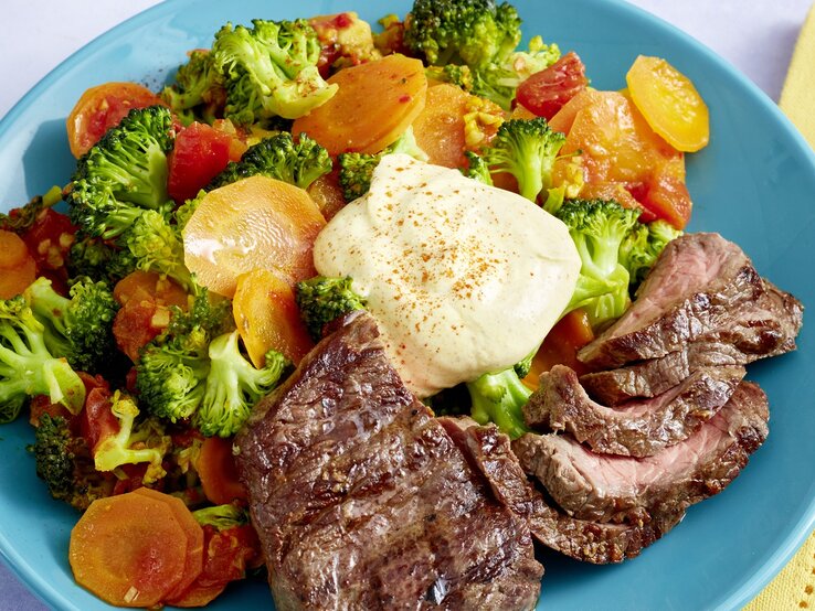 Hüftsteak mit Brokkoli-Möhren-Mix und griechischem Joghurt auf rundem Teller / Draufsicht, schräg