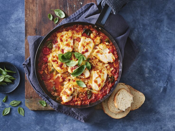 Eintopf mit Hackfleisch und Halloumi / runde Schüssel / drei Scheiben Weißbrot / frische Kräuter / Untergrund Holzbrett 