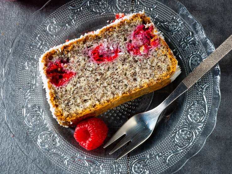 Mohnkuchen mit Himbeeren / eine Scheibe vom kastenkuchen / runder Teller aus Glas / eine frische Himbeere / Kuchengabel / Draufsicht