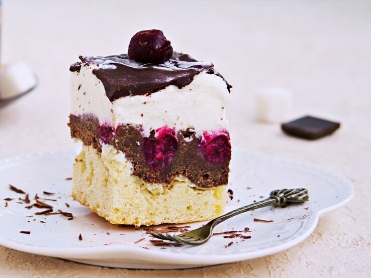 Ein Stück der Donauwelle auf einem Teller mit hellem Untergrund und einer Tasse Kaffee daneben.