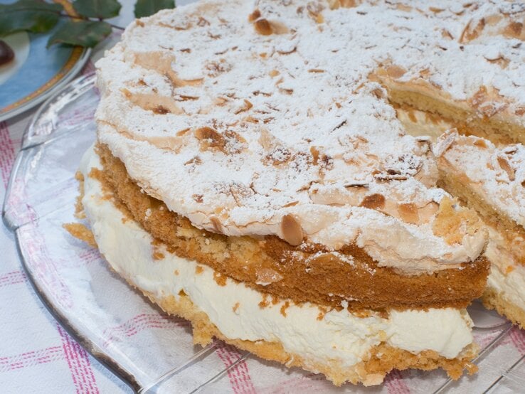 Die Sahnetorte mit Baiserschicht und mandeln auf einem Tisch mit rot-weiß-karierter Tischdecke