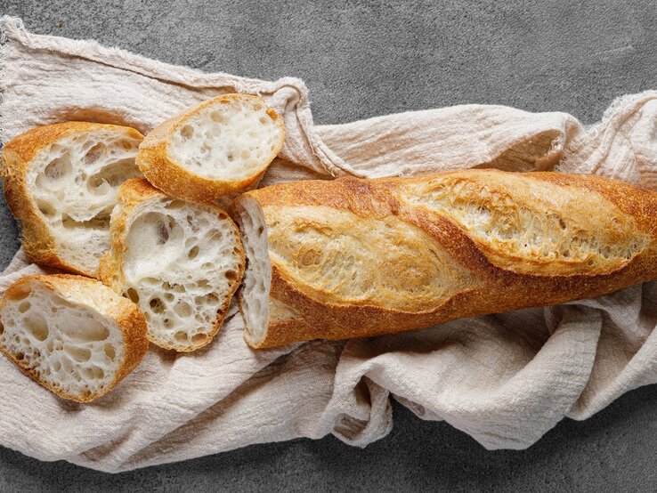 Das Baguette auf einem grauen Tisch mit beiger Tischdecke. Alles von oben fotografiert.