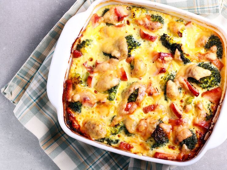 Blick von oben auf eine weiße Auflaufform, in der ein Brokkoli-Schinken-Gratin zubereitet wurde. Die Auflaufform steht auf einem grau-grün karierten Tuch.