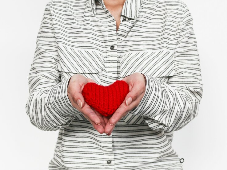 Frau hält ein rotes gestricktes Mini-Herz in ihren Händen