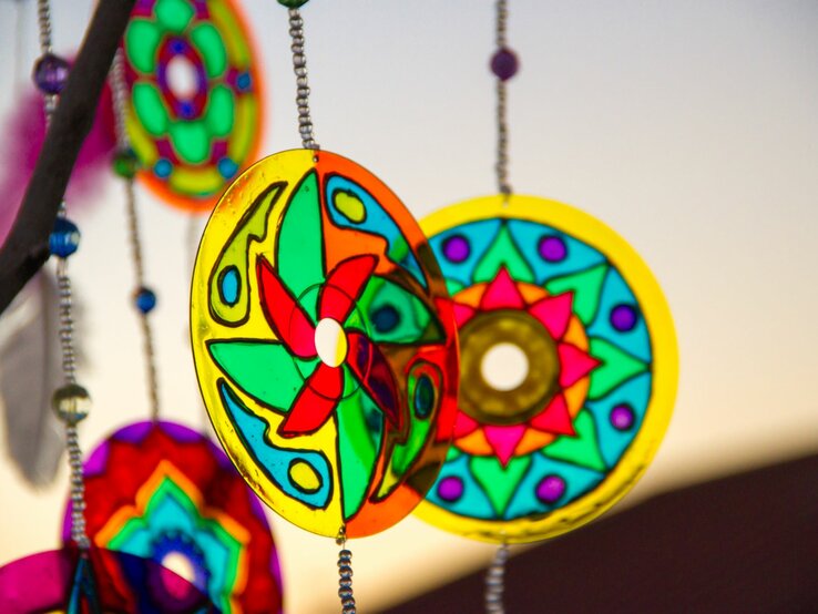 Glänzende, runde CDs mit leuchtenden Farben und Mustern hängen an einer Perlenkette im Abendlicht.