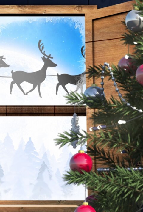 Ein Holzfenster mit einem weihnachtlichen Fensterbild, das eine winterliche Landschaft mit schneebedeckten Tannen und einem vorbeiziehendem Rentierschlitten zeigt.