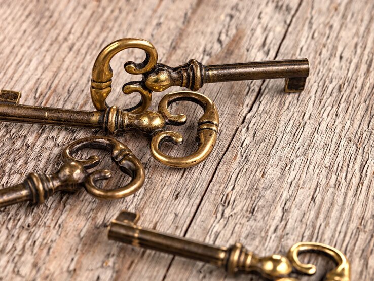 Vier antike Messingschlüssel mit kunstvoll verzierten Griffen liegen auf einer rustikalen Holzoberfläche.