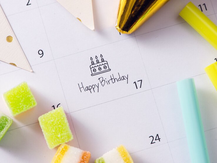 Ein Kalender mit der Markierung "Happy Birthday" am 17., umgeben von bunten Süßigkeiten, Partyhüten und Dekoration.