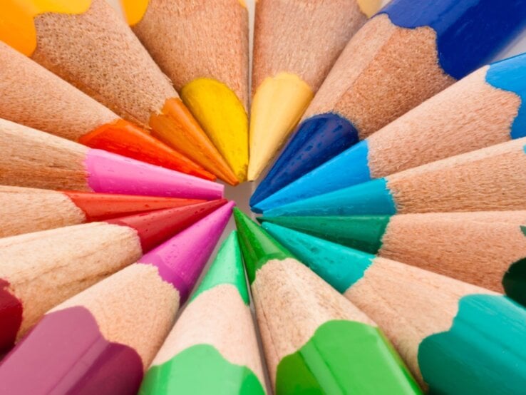Bunte Buntstifte in kräftigen Farben liegen mit den gespitzten Spitzen fächerförmig auf weißem Hintergrund.