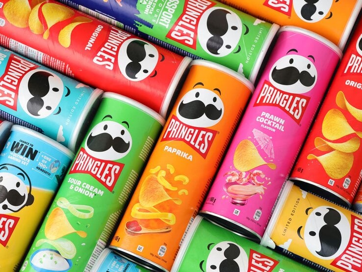 Bunte Pringles-Dosen in verschiedenen Geschmacksrichtungen wie Paprika, Sour Cream und Prawn Cocktail liegen nebeneinander aufgereiht.