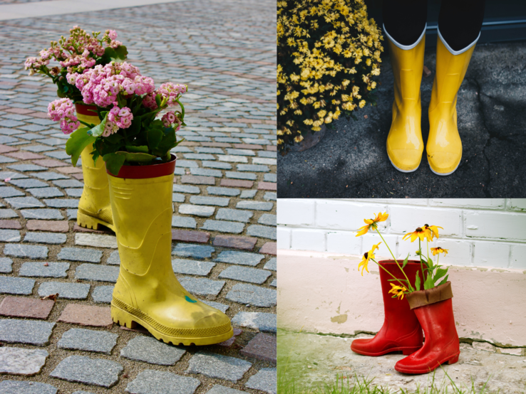 Zwei gelbe Gummistiefel mit pinken Blumen auf Pflastersteinen, daneben rote Stiefel mit Sonnenhutblüten vor heller Wand.