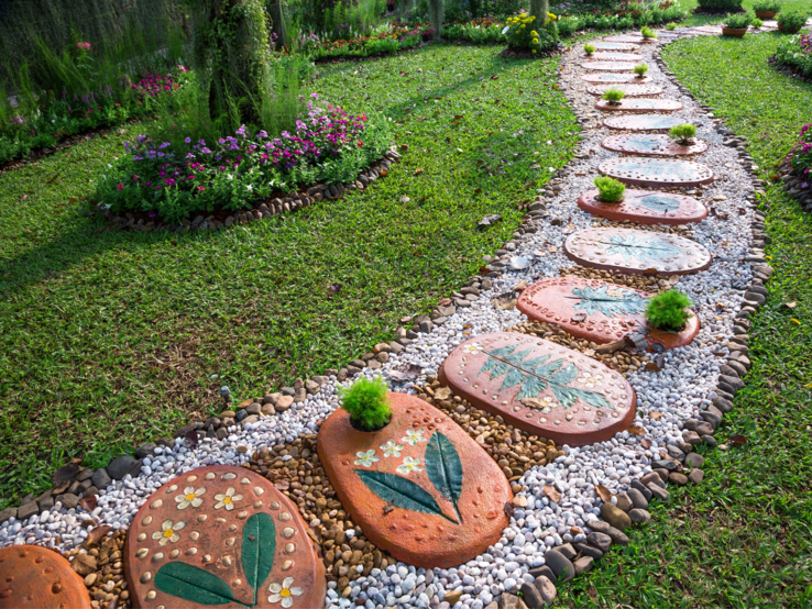 Geschwungener Gartenweg aus bunten Trittsteinen mit Blumenmotiven, umrahmt von Kieseln und gepflegtem Rasen.