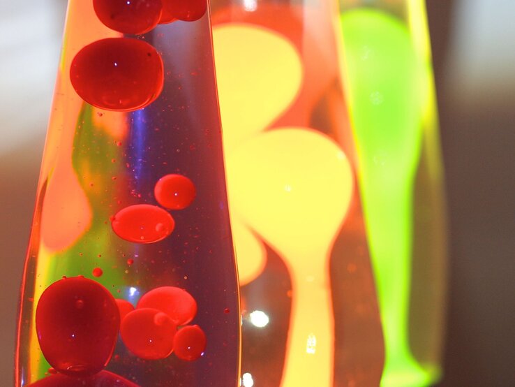 DIY Basteln Lavalampe Drei Lavalampen mit leuchtend roter, gelber und grüner Wachsmischung blubbern bunt in flüssigem Licht vor dunklem Hintergrund.