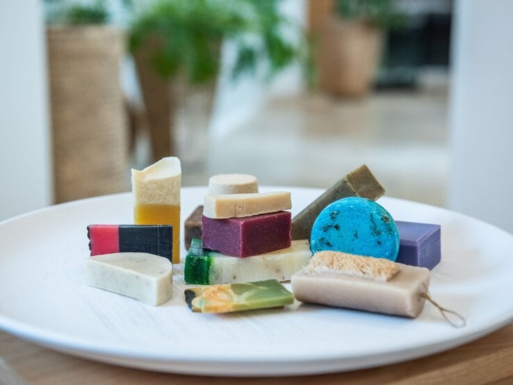 Bunt gemischte handgemachtes Shampoo in verschiedenen Formen und Farben liegen dekorativ auf einem weißen Keramikteller.