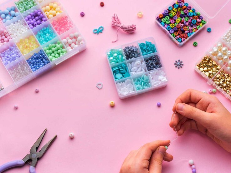 DIY-Bastel-Ideen unter 20 Minuten Erstellen von buntem Perlenschmuck mit verschiedenen Perlen und Bastelwerkzeugen auf einer hellrosa Oberfläche