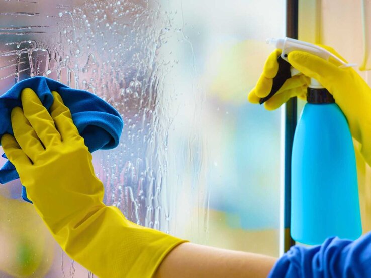 Frau putzt Fenster mit Handschuhen - Nahaufnahme
