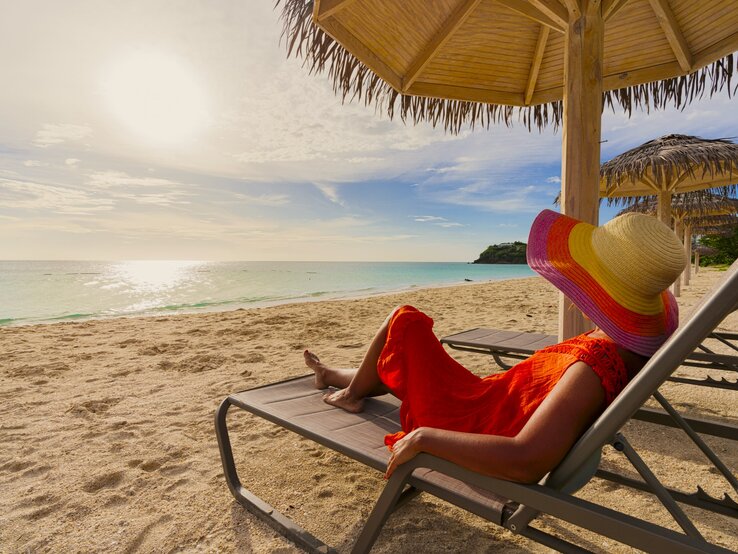Zu sehen ist eine Frau mit Sonnenhut, die am Strand liegt