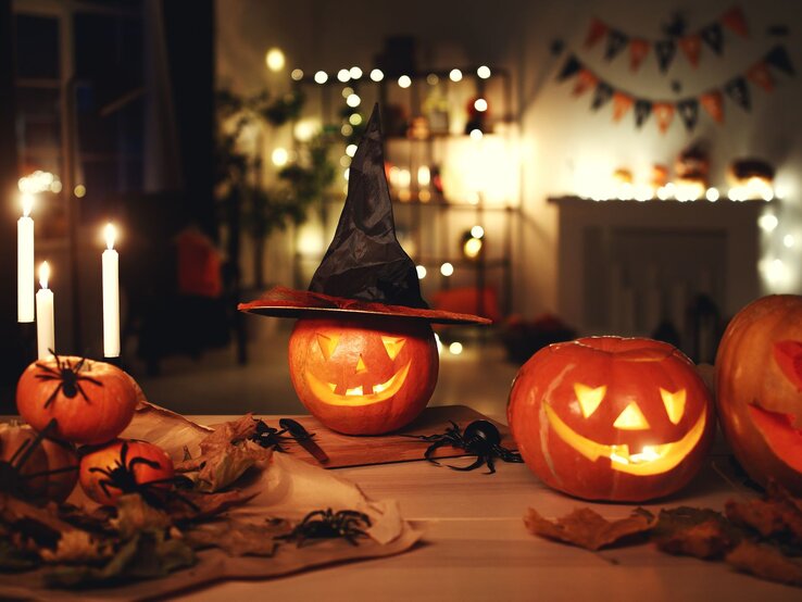Solarleuchte Halloween DIY Solarleuchten basteln: Drei leuchtende Kürbislaternen mit geschnitzten Gesichtern, einer mit Hexenhut, auf herbstlich dekoriertem Tisch bei Kerzenlicht.