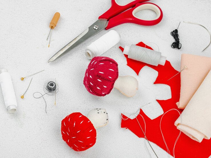 Pilz-Laterne basteln  Materialien zum Basteln einer Pilz-Laterne: Filzpilze, Stoff, Garnrollen, Schere und Nadeln auf hellem Untergrund.