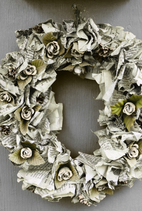 Bunter Türkranz aus gelbem, rotem und grünem Papier hängt an weißer Tür, daneben Kranz aus Zeitungspapier und Tasse Kaffee.