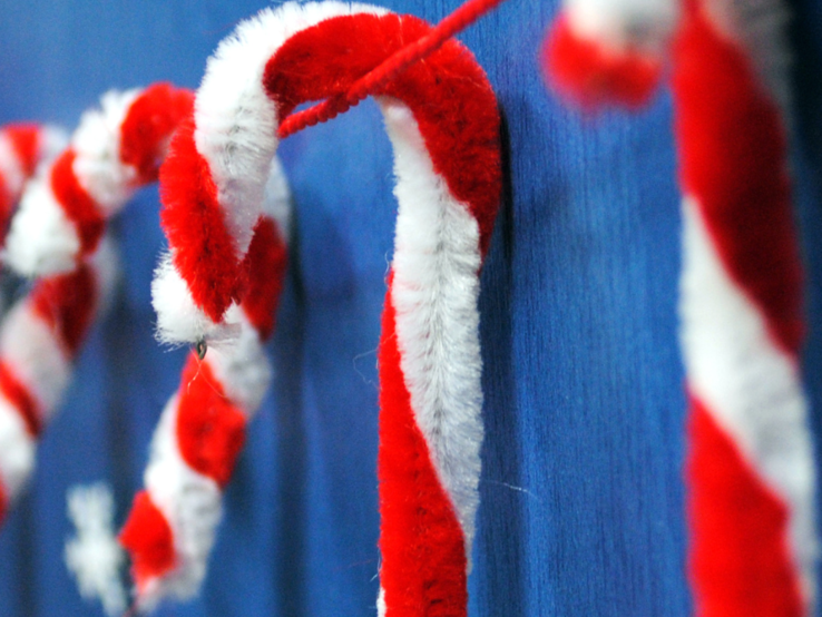 Bunte Weihnachtsdeko aus Pfeifenreinigern: Zuckerstangen, Sterne, Schneemänner, Kränze und Bastelmaterial auf Tischflächen.