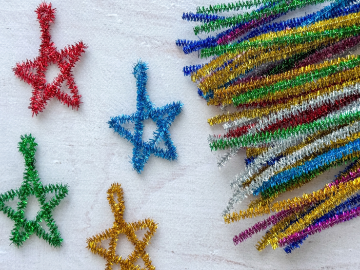 Bunte Weihnachtsdeko aus Pfeifenreinigern: Zuckerstangen, Sterne, Schneemänner, Kränze und Bastelmaterial auf Tischflächen.