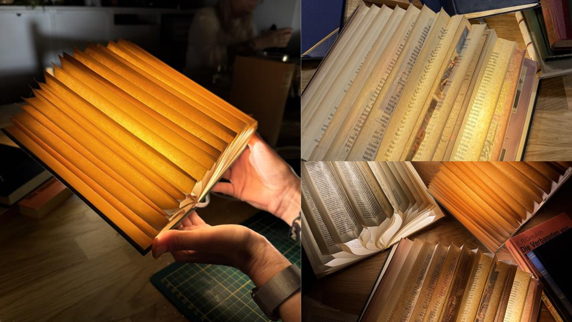 Mehrere kunstvoll gefaltete, warm leuchtende Buch-Lampen aus alten Seiten liegen auf einem Holztisch, eine wird gerade in Händen gehalten.