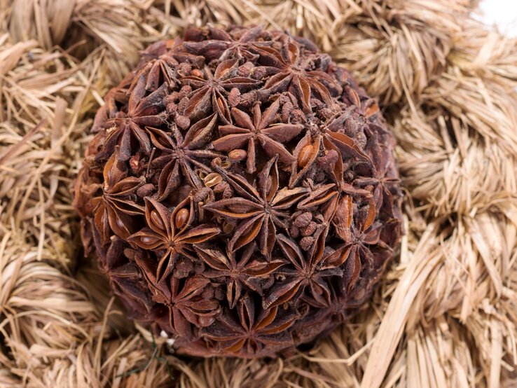 Runde Kugel aus getrocknetem Sternanis und Gewürznelken liegt dekorativ auf einem Nest aus hellem Strohgeflecht