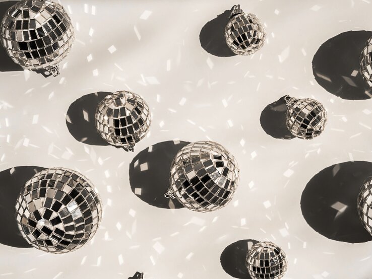 Mehrere glänzende Discokugeln werfen tanzende Lichtreflexe und runde Schatten auf einen hellen Untergrund.