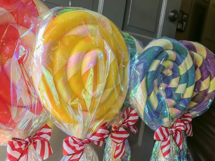 Vier riesige Lollis aus bunt gewickelten Poolnudeln mit Zellophan umhüllt und rot-weiß gestreiften Schleifen verziert.