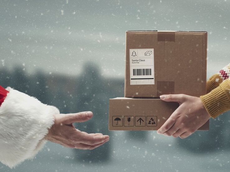 Eine Person im Rentierpulli übergibt im Schneetreiben zwei Pakete an einen Mann im roten Santa-Mantel mit weißem Kunstpelz.