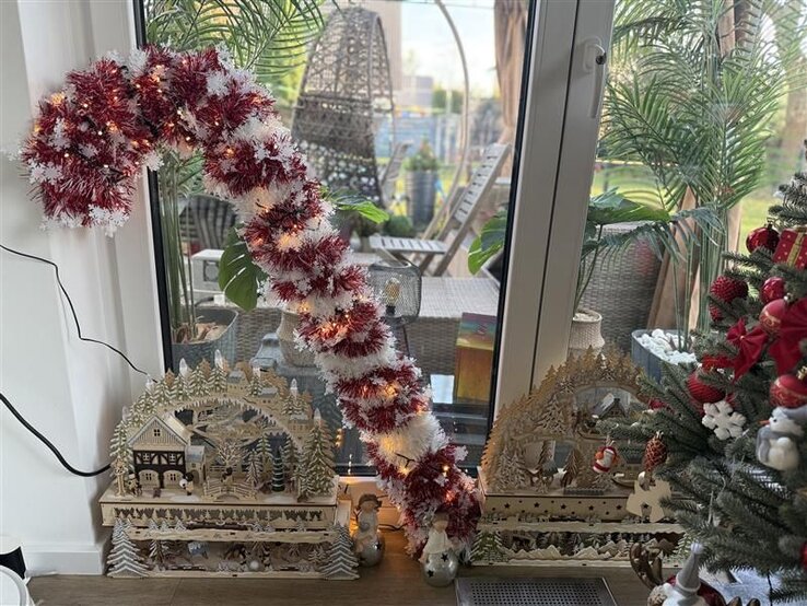 Riesige Zuckerstange aus HT-Rohren und roter und weißer Lichtergirlande steht leuchtend neben weihnachtlichen Holzszenen am Fenster. | © Madeleine Liedke 