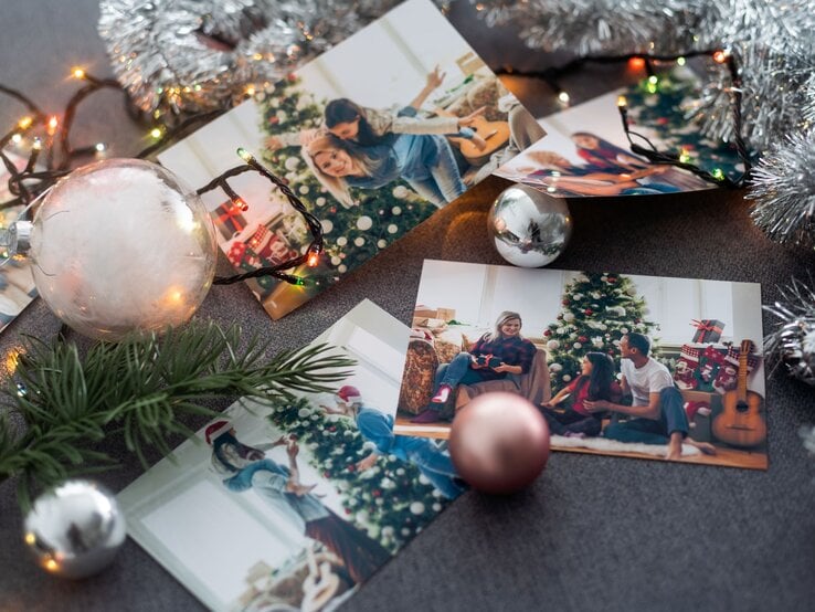 Weihnachtsfotos auf dunklem Stoff, umgeben von Kugeln, Lichterkette, Tannenzweig und silberner Girlande arrangiert.