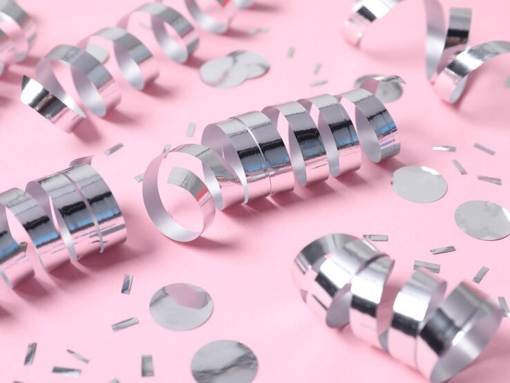 Silberne Luftschlangen und Konfetti liegen dekorativ auf rosa Untergrund und funkeln im weichen Licht.